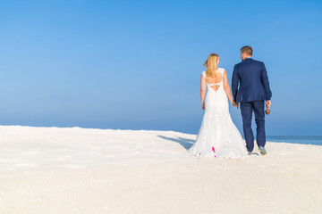 Fototapeta na wymiar Bride and groom walking away on the beach, romantic background concept