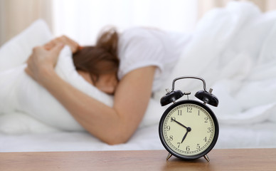 Beautiful sleeping woman lying in bed and trying to wake up with alarm clock. Girl having trouble with getting up early in the morning, Nightmare