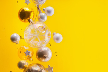 Silver and golden christmas bubbles and stars flying on yellow background with copy space
