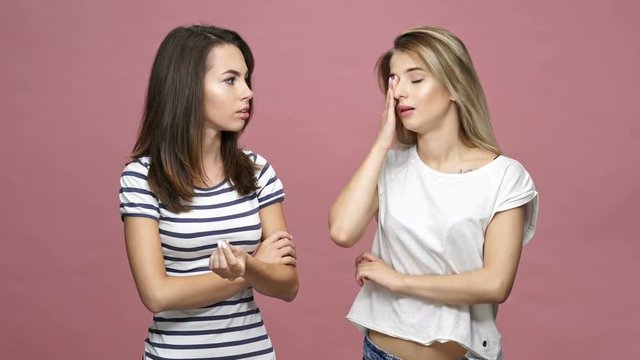 Two displeased frends ladies talking and discussing isolated over pink