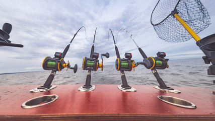 Ausrüstung zum Angeln mit Angelruten und Multirollen zum Schleppfischen in Halterung vom Boot auf dem Wasser im See oder Meer mit Kescher und Downrigger © annieze