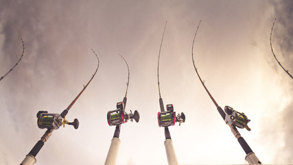Angelruten mit Rollen zum Schleppangeln aufgereiht auf Boot im Wasser auf See oder Meer in Halterung zum Angeln bei wolkigem Himmel © annieze