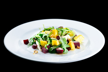 Delicious and appetizing salad with beetroot and fruit mango in a white plate isolated on black background. Autumn menu in an Italian restaurant. Photo for menu design