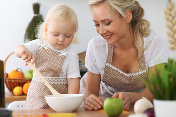 Obraz na płótnie Canvas Mother and little daughter are cooking in the kitchen. Spending time all together or happy family concept
