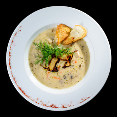 Tasty mushroom cream soup with parsley and spices in a white plate served with toast bread, isolated on black background. Top view, flat, overhead. Autumn menu in an Italian restaurant