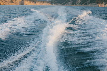 estela de barco sobre mar azul y linea de la costa al fondo.