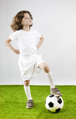 Young football player playing soccer on the grass. Gray background.