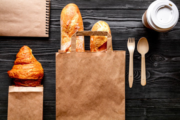 cup coffee and bread in paper bag on wooden background