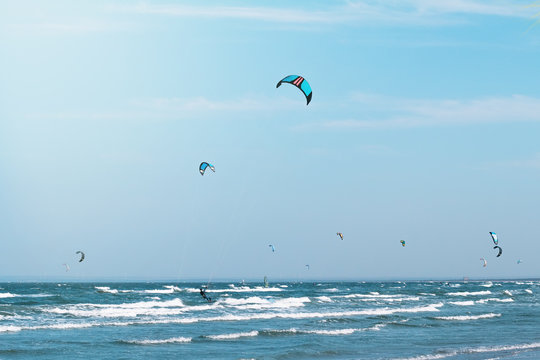 Kitesurfing in the wavy sea. Many kitesurfers on the sky background.