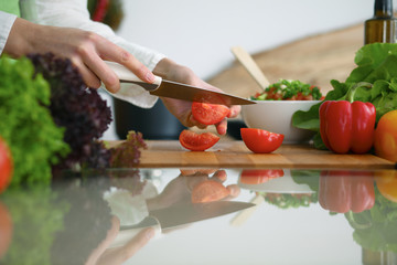 Closeup of human hands cooking vegetables salad in kitchen on the glass  table with reflection