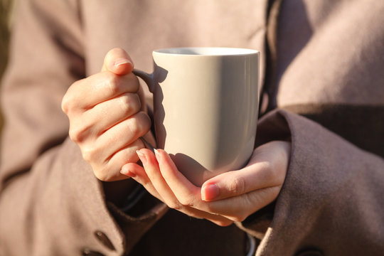 Closeup view of disposable cup of coffee or tea in womans hand. Autumn park with trees and yellow leafes