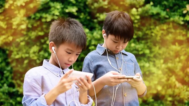 Slow motion of preteen Asian Thai boy is using smartphone to play game in his home garden. Technology and health concept