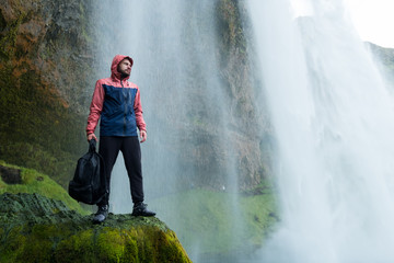 Fototapeta premium Adventure man by skogafoss waterfall, nature on Iceland. Young man visiting nature landscape.