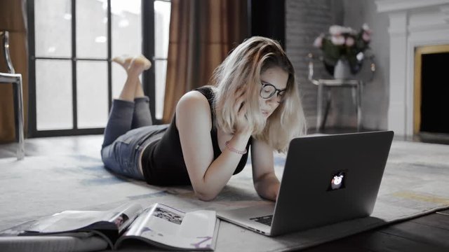 Blonde woman lying on floor room talking on mobile in front laptop