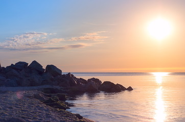stone beach on the sea shore. blue sky horizon. reflection of the sunrise. Toned