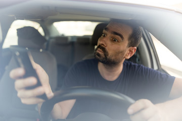 Man texting while driving.  Using a smartphone while driving.  Front view of man driving while using mobile phone.