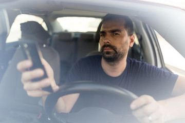 Man texting while driving.  Using a smartphone while driving.  Front view of man driving while...