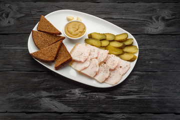 Traditional snacks for vodka: onion, lard, pickled cucumbers, garlic and mustard. Dark wooden background.