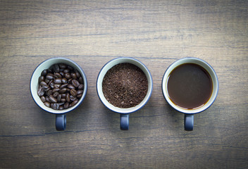 Three cups of difference stages of coffee preparation or the making of coffee drink isolated on brown wooden surface