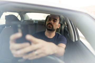 Man texting while driving.  Using a smartphone while driving.  Front view of man driving while...
