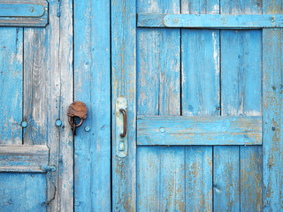 Ancient wooden gate closed on a rusty padlock, painted with old peeling light blue paint. Rural building background