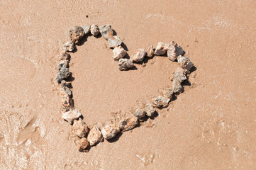 Heart lined with stones on the sandy beach of the sea