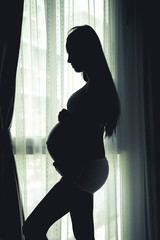 Pregnant young woman beside the window in bedroom waiting the the new born of her child with happy and excited