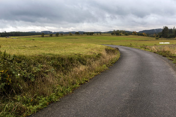 a narrow road leading between fields under storm clouds in autumn