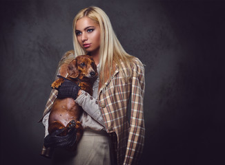 A stylish blonde female holds a red badger dog.