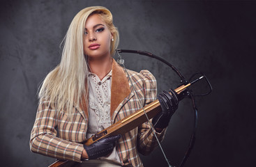 Studio portrait of blond old fashioned female holds a crossbow.