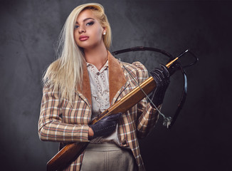 Studio portrait of blond old fashioned female holds a crossbow.