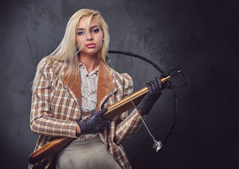 Studio portrait of blond old fashioned female holds a crossbow.