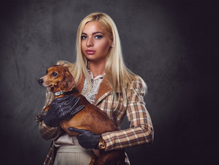 A stylish blonde female holds a red badger dog.