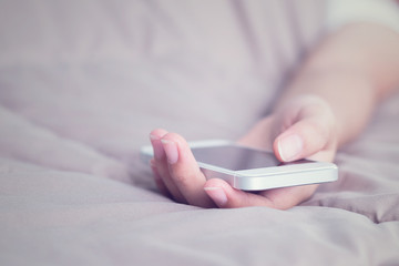 Woman hand with mobile phone sleeping on bed.