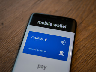 Credit card in smart phone. Mobile wallet concept app. Pay with your smartphone. Close up on wood background, selective focus.