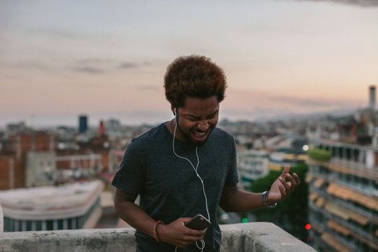 African american man listening to music with his smartphone and dancing on a rooftop at sunset.