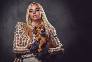 A stylish blonde female holds a red badger dog.