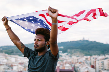 Young black man waving an american flag outdoors.