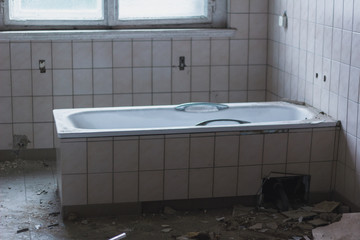 An eery bathroom in an abandoned insane asylum with an intact bathtub in the center.