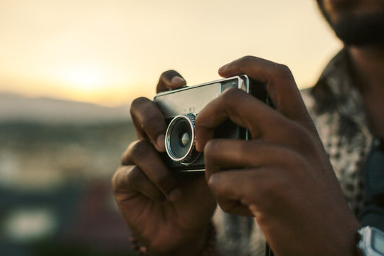 Young black man taking a photo with an old camera at sunset.