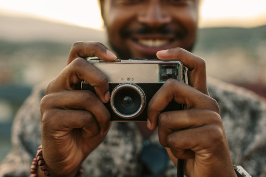 Young black man taking a photo with an old camera at sunset.