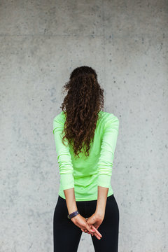 Back view of a young african american woman doing stretching exercises in front of a wall.