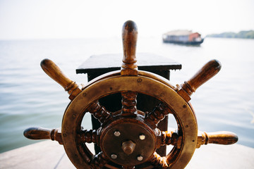 Old boat steering wheel in the sea with boat in the background. Kerala backwaters, India.