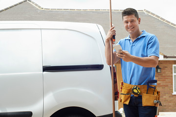 Portrait Of Plumber With Van Texting On Mobile Phone Outside House - obrazy, fototapety, plakaty