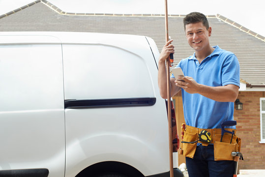 Portrait Of Plumber With Van Texting On Mobile Phone Outside House