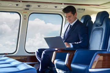 Businessman Working On Laptop In Helicopter Cabin During Flight