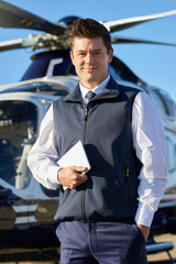 Portrait Of Pilot Standing In Front Of Helicopter With Digital Tablet