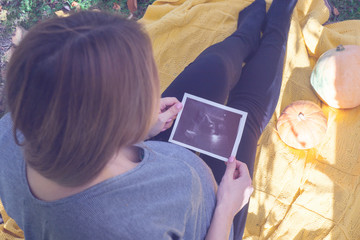 Fototapeta premium Pregnant woman looking at ultrasound scan of baby, close up of scan, autumn time