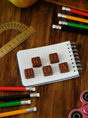 School supplies and the word school in Russian laid of chocolate cubes on a wooden table