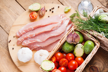 Slices of raw pork meat and wicker basket with vegetables 